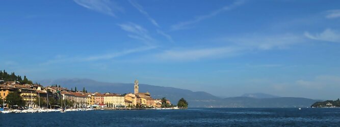 Club Reisen beliebte Urlaubsziele am Gardasee -  Mit einer Fläche von 370 km² ist der Gardasee der größte See Italiens. Es liegt am Fuße der Alpen und erstreckt sich über drei Staaten: Lombardei, Venetien und Trentino. Die maximale Tiefe des Sees beträgt 346 m, er hat eine längliche Form und sein nördliches Ende ist sehr schmal. Dort ist der See von den Bergen der Gruppo di Baldo umgeben. Du trittst aus deinem gemütlichen Hotelzimmer und es begrüßt dich die warme italienische Sonne. Du blickst auf den atemberaubenden Gardasee, der in zahlreichen Blautönen schimmert - von tiefem Dunkelblau bis zu funkelndem Türkis. Majestätische Berge umgeben dich, während die Brise sanft deine Haut streichelt und der Duft von blühenden Zitronenbäumen deine Nase kitzelt. Du schlenderst die malerischen, engen Gassen entlang, vorbei an farbenfrohen, blumengeschmückten Häusern. Vereinzelt unterbricht das fröhliche Lachen der Einheimischen die friedvolle Stille. Du fühlst dich wie in einem Traum, der nicht enden will. Jeder Schritt führt dich zu neuen Entdeckungen und Abenteuern. Du probierst die köstliche italienische Küche mit ihren frischen Zutaten und verführerischen Aromen. Die Sonne geht langsam unter und taucht den Himmel in ein leuchtendes Orange-rot - ein spektakulärer Anblick.